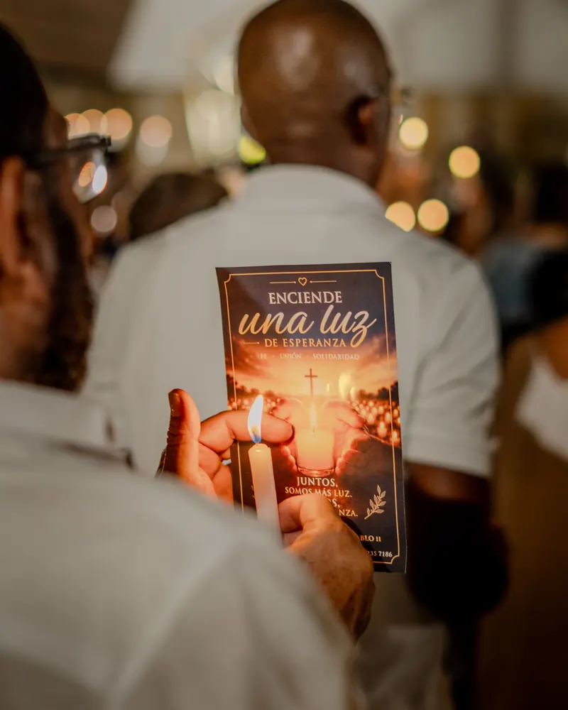 Manos que sostienen una vela encendida y la tarjeta «Enciende una luz de esperanza»